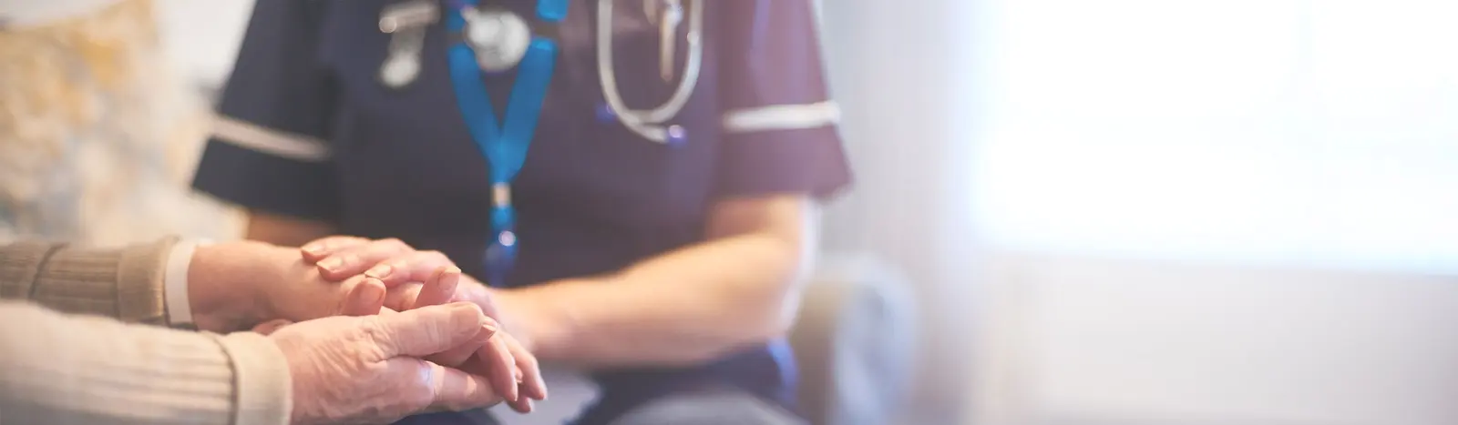 A nurse gently holds the hands of an elderly patient
