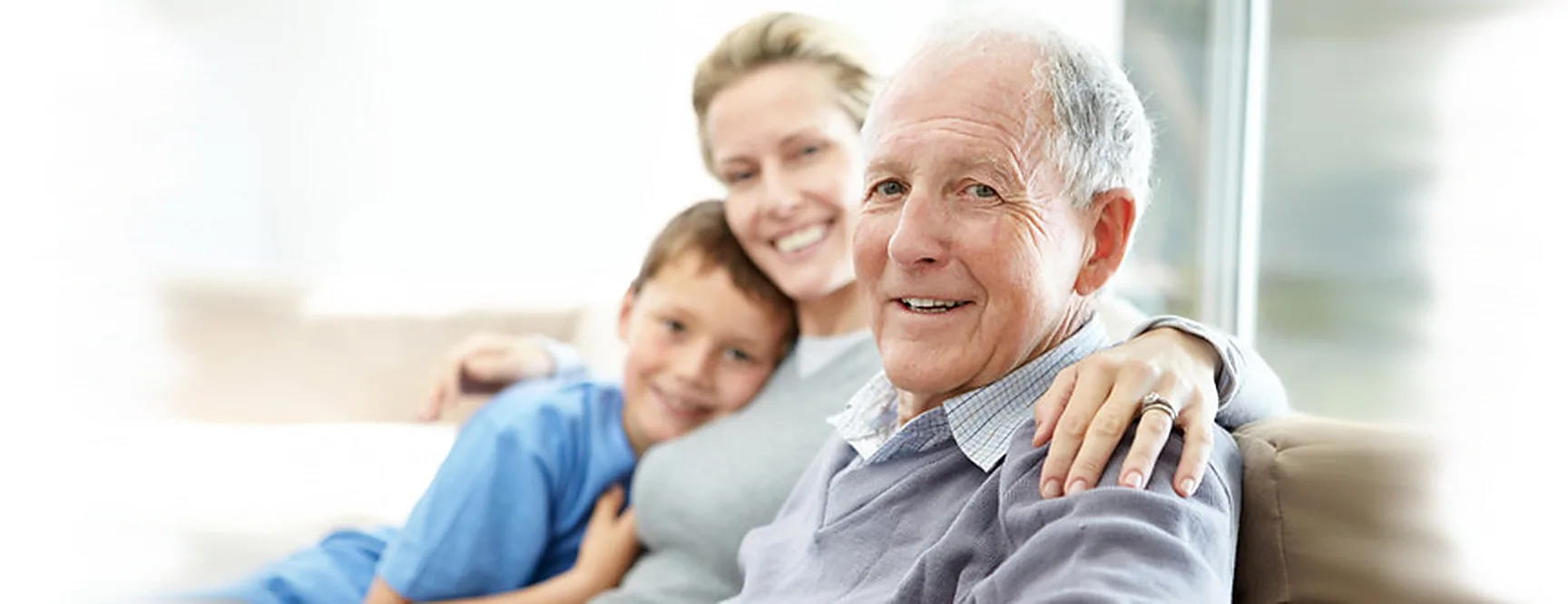 A smiling older man sitting on a couch with a woman and a young boy